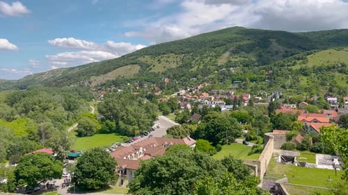 A picturesque village surrounded by lush green hills under a bright blue sky with scattered clouds.
