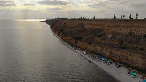 Rays of Setting Sun Break Through Clouds Over Sea Coast with Vacationing Travelers