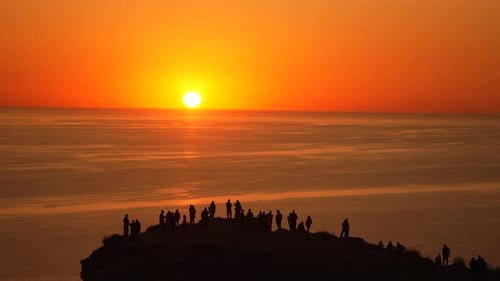 Silhouettes de foule au coucher du soleil regardant un magnifique coucher de soleil orange sur l'océan depuis une colline