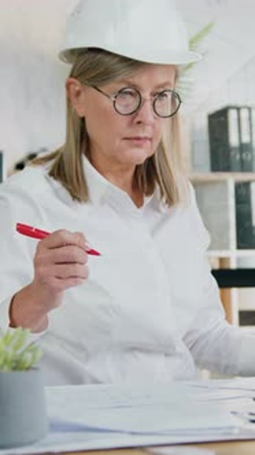 Woman Architect Inspects Blueprints in Office with Hardhat