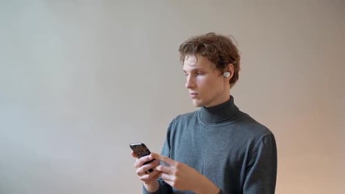 Young Adult Using Smartphone With Wireless Earbuds
