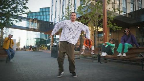 Young And Stylish Male Hip Hop Dancer Is Freestyling On City Street Among Modern Buildings In the
