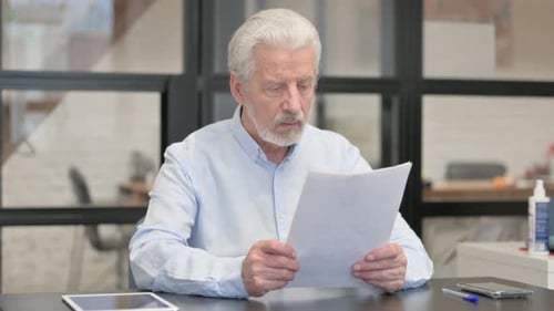 Senior Man Reviews Documents at Office Desk
