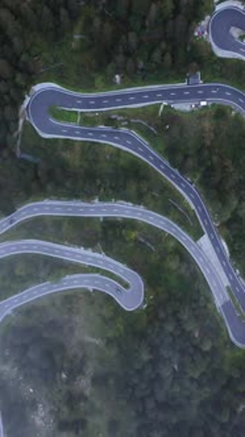 Vertical drone shot above traffic on a winding road, foggy day in the alps