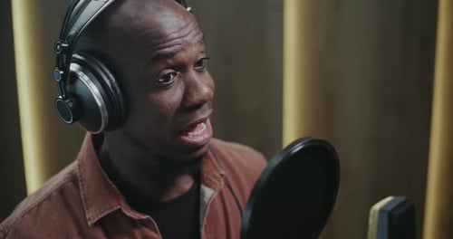 Man Wearing Headphones Speaking Into Microphone In Studio