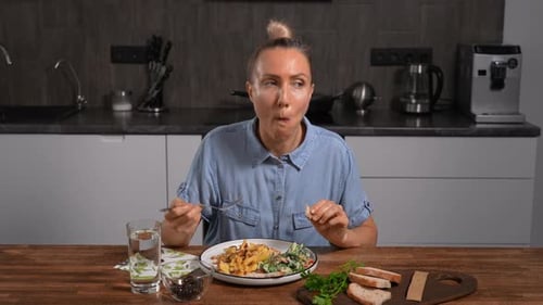 A Woman is Sitting at a Wooden Table in a Modern Kitchen Eating a Homemade Meal On the Plate are