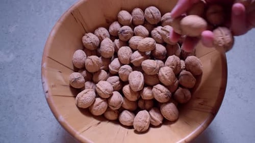 Dried walnuts in a wooden bowl. Throwing some walnuts in the bowl.