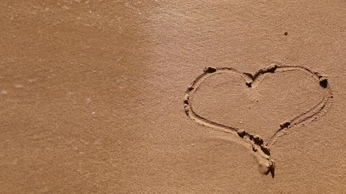 handwritten, drawn heart on golden sand, on the beach washed away by a wave on the sea or ocean.