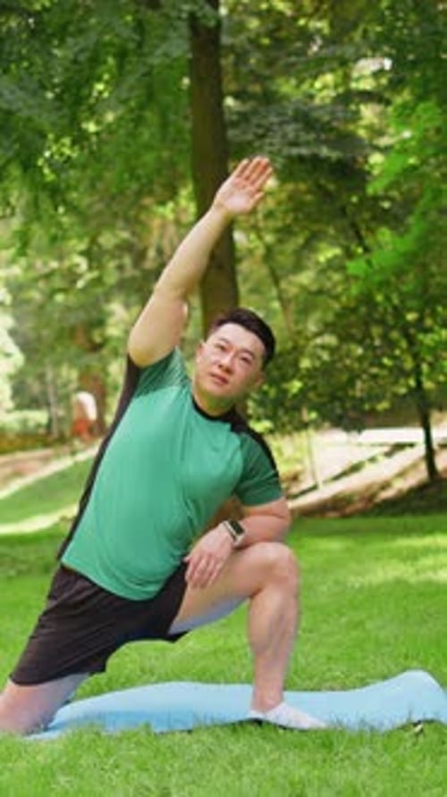 Adult Asian Sportsman Guy Does Gymnastics Practices Yoga Performs Exercises on Mat in City Park