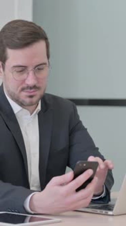 Man Working on Phone and Laptop in Office