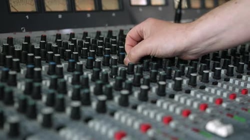 Recording studio engineer turning a knob on a mixing desk console