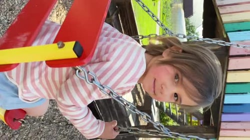 Vertical Video a Little Girl Rides on a Swing Her Hair Flutters in the Wind