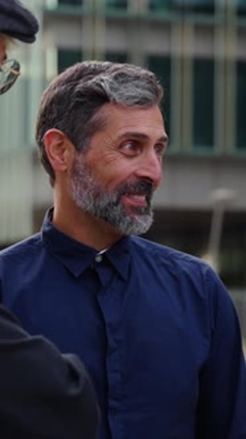 Mature Grey Man Talks Animated with Young Coworkers Outdoors