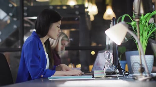Video of asian businesswoman working at a laptop at night in office with female colleague