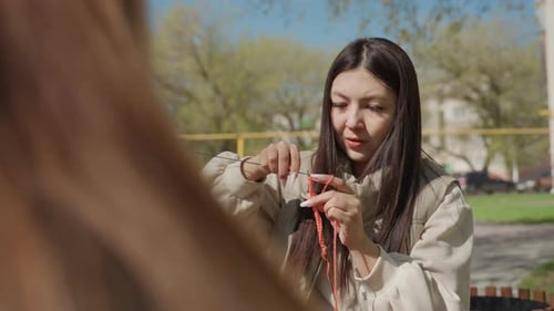 Asian Mentor Teaching Knitting During Park Chat Midshot Showing Instructor Guiding Hands and