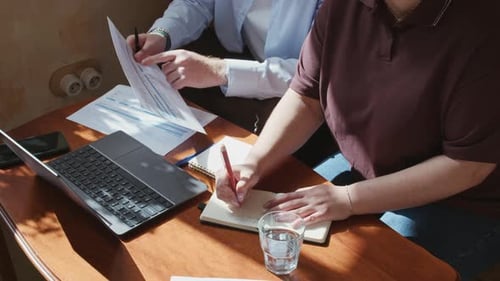 Business Partners Reviewing Financial Documents at Table with Laptop in Cafe