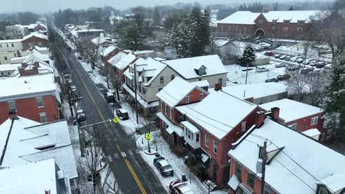 Aerial view of snowflakes falling on quaint small town in America. Establishing shot of snowstorm on