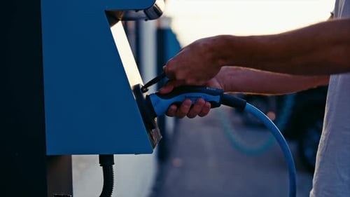 Close Up Hand Plugging Blue Power Cable Into Charging Station