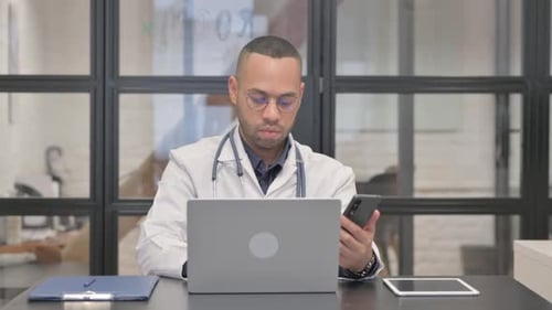 Doctor Uses Cell Phone at Desk in Office