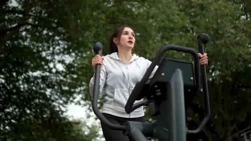 Woman Enjoys Outdoor Workout on Fitness Equipment in Park During Daylight Focusing on Her Exercise