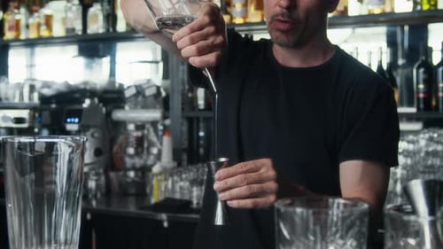Homme mûr versant de la vodka dans un jigger tout en préparant un cocktail au comptoir du bar