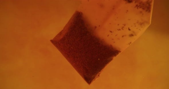 Close up of tea bag diffusing in a clear glass. Macro slow motion shot ...