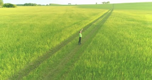 Sporty Child Standing in Green Wheat Field with Raised Hands Up