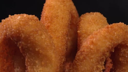 Crunchy onion rings in batter on dark background. Ideal for fast food ads, takeout snacks