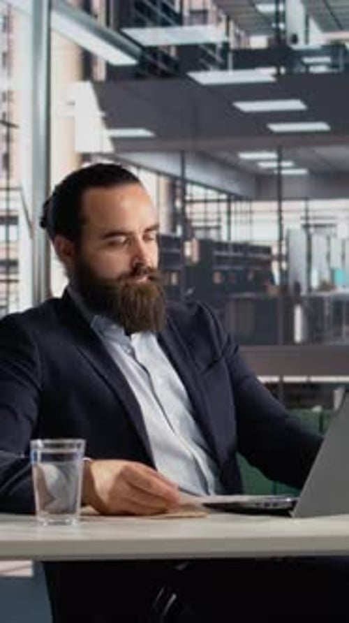 Vertical Video Male CEO Engaged in Reviewing Organizational KPIs on Documents and Laptop