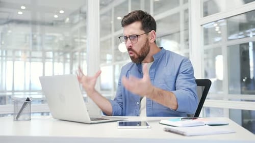 Frustrated Man Arguing on Laptop in Bright Office