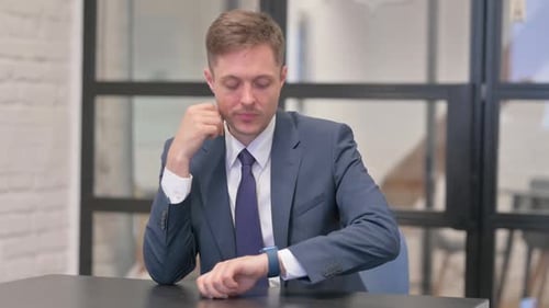 Man Thinking at Desk Checks His Smart Watch