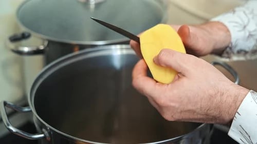 Descascando uma batata sobre uma panela Uma pessoa está descascando uma batata sobre uma panela na cozinha preparando uma refeição