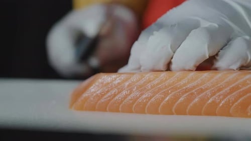 Female chef hand using fish fillet knife slice fresh salmon meat on cutting board in restaurant