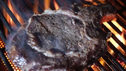 Beef Steak on Fire Coals on Iron Grill in Flame of Smoke Barbecue Meat on Grill Roasting Meat Steak