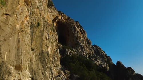 Luftbild, das in der Nähe einer Mauer in Richtung einer in einen Berg gehauenen Höhle in Griechenland fliegt