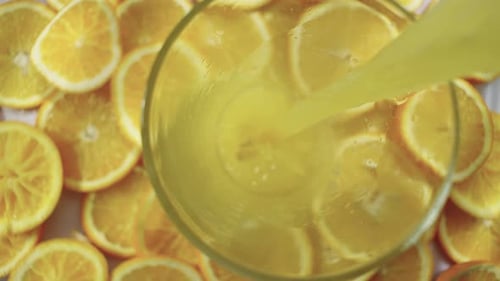 Orange Juice Being Poured into Glass with Orange Slices