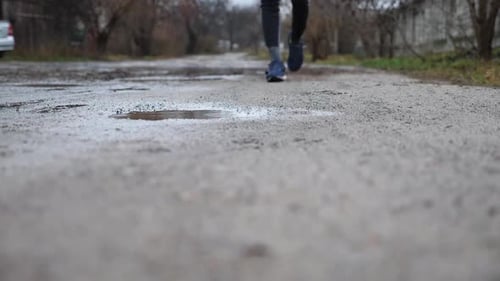 Legs of Young Sportsman Stepping Into Puddle While Jogging Along Rural Trail Male Feet of Sporty Man