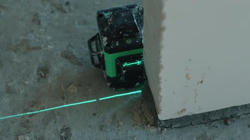 Lasernivellierung, die während der Bauarbeiten aus nächster Nähe eine grüne Ausrichtungslinie in die Nähe der Wand projiziert