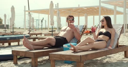 Cheerful Couple with Cocktails Sunbathing on the Beach