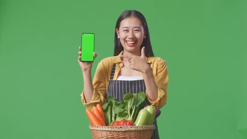 Farmer With Vegetable Basket Showing And Pointing To Green Screen Mobile Phone On Green Screen