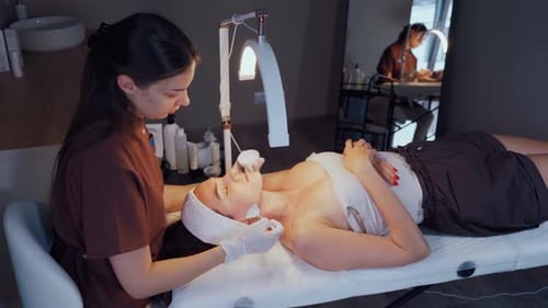 Beautician Cleansing Woman's Face During Facial Treatment