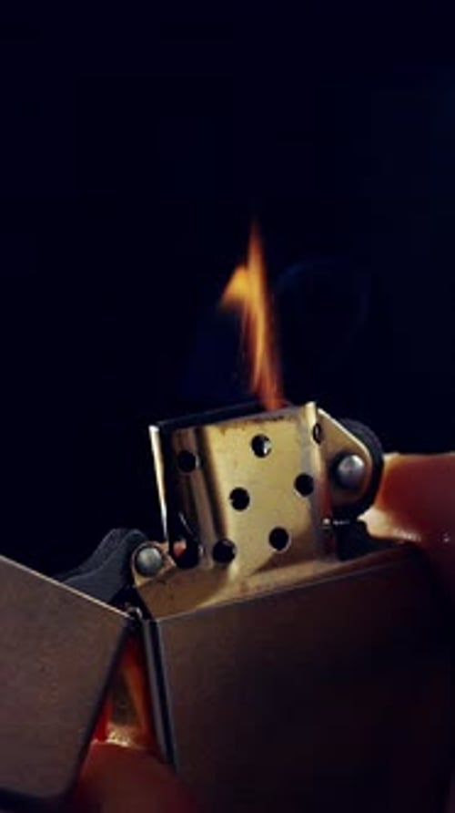 Gros plan d'un briquet en métal qui émet des étincelles et allume une flamme au ralenti sur fond noir.