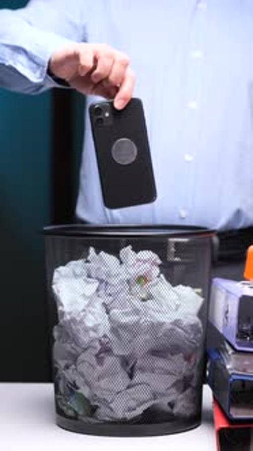 Vertical Video Discarding Smartphone Into Trash Bin at Office Desk