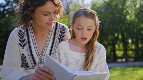 Girl and Woman Reading Book Together in Park