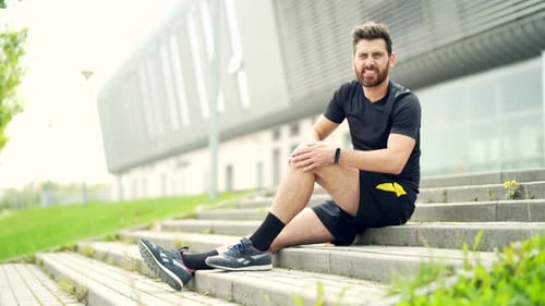 Athletic Man Holds His Knee in Pain Outdoors
