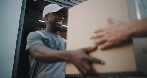 Worker Giving Cardboard Box to Unrecognizable Colleague Smiling and Looking at Camera