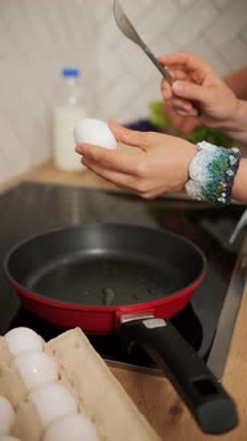 Female Hands Breaking an Egg Over a Frying Pan with a Knife