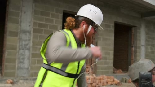 Trabalhador construtor concluiu o trabalho, dança e ouve música em fones de ouvido andando no canteiro de obras.