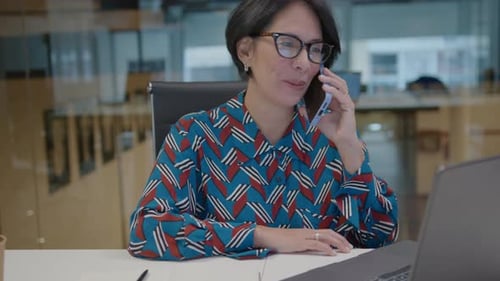 Mature Businesswoman Using Laptop and Speaking on Phone in Office