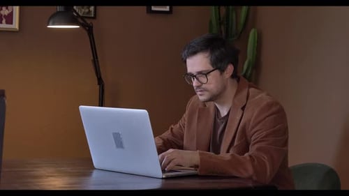 Kaukasischer Mann arbeitet zu Hause aus der Ferne am Tisch mit Laptop und sitzt im Wohnzimmer